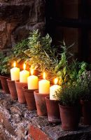 Candles in terracotta pots on windowsill with potted herbs - The Oast Houses, Hampshire