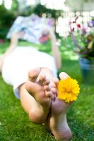 Woman lying on lawn looking at magazine with yellow flower between her toes