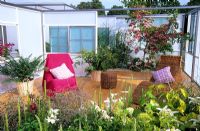 Outdoor room with decking, a wicker chairs, planters and Cornus kousa 'Satomi'. 'A Woman's Sanctuary' garden designed by Sarah Eberle at RHS Hampton Court Flower Show.