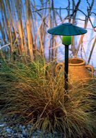 Light in garden illuminating ornamental grass and pot