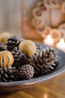 Festive arrangement of pine cones and dried oranges in wooden bowl with candles in the background