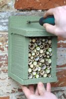 Step by step 7 of making a bug house for hiberating insects out of reclaimed timber - Putting up the bug box on a sheltered wall