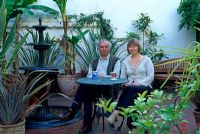 Angela and Robin sitting in tiled conservatory area beside fountain - Tipton Lodge, Devon, UK