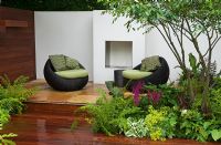 Round wicker chairs with green cushions in front of outdoor fireplace with ferns and Astilbe in the foreground in the Formal Elements Garden - RHS Hampton Court Flower Show 2008
