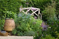 Wooden bench in gravel area with empty terracotta urn with Nigella, Alliums and Geranium plamatum - Eldenhurst