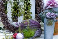Frosted savoy cabbage and ornamental kales with Christmas baubles on bench with mistletoe