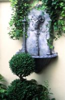 Wall mounted ram's head water feature in faux lead, Buxus topiary, Busy Lizzies and Hedera in trough