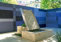 San Francisco garden, the courtyard walls are striking, fininshed in irregular shaped panels of varying shades of blue. A water feature with water falling over an antique sculptured panel into the raised pond.