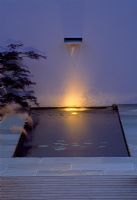 Water feature and pond in a minimal garden, painted wall and night lighting with Acer