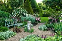 Formal garden with blue painted wrought iron bench, old sundial, gravel paths, roses, herbaceous perennials and view to lawns with box hedging and Yew topiary - Cerne Abbas, Dorset