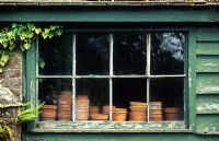 Vintage terracotta flower pots on bench of rustic potting shed. Peeling old paint on weather boarding - Cerne Abbas, Dorset