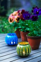 Pansies in terracotta pots on a wooden garden table with tealights in the foreground