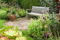 Wooden bench with cobble patio and Darmera peltata, Molinia caerulea 'Variegata', Allium sphaerocephalon, Eryngium plenum, Amaranthus 'Red Hopi Dye' and Sedum 'Autumn Joy' - Southlands, NGS garden, Lancashire