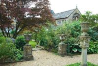 Acer japonicum spreads over garden full of architectural fragments, backed by Romanesque chapel. Private garden, Dorset, UK