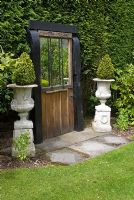 Mirrored door embedded in conifer hedge, and adjacent classical urns containing clipped Buxus at Aureol House, Lancashire