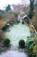 Long narrow town garden divided into sections. Formal design with lawn and box topiary nearest house leading to small woodland garden with group of birch trees and small shed. January.