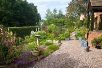A plant lovers cottage garden with herbaceous perennials, metal containers with shaped box and hedging, a sun-dial with gravel path at Coley Cottage, NGS, Little Haywood, Staffordshire 