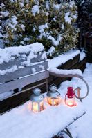 Three tea light candle lanterns set in snow on garden bench