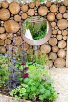 Detail of Moongate in recycled log wall with border of Geranium sylvaticum 'Narratives of Nature' garden at Future gardens, St Albans, Herts 