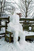 Snowman made by children, sitting on garden bench