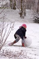 Child rolling a ball of snow to make a snowman in February