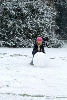 Child rolling a ball of snow to make a snowman in February
