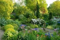May garden with gravel area and wooden ornament, natural pond and fastigiate conifers. Hillbark, Bardsey, Yorkshire NGS