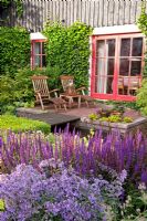 Patio in country garden with wooden loungers. Borders of Nepeta nervosa and Salvia nemorosa 'Caradonna'