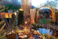 Winter garden with pond lit up at dusk

