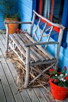 Rustic wooden bench on the veranda of a blue painted cottage. Impatiens in red pot. No. 11, Christchurch, New Zealand