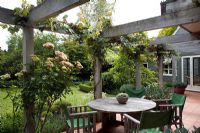 Dining area under wooden pergola with Vitis vinifera 'Purpurea' and Rosa 'Greensleeves'. Christchurch, New Zealand