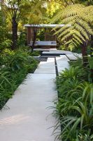 Large paved stepping stones cross water towards a pavilion bordered by tropical planting and tree ferns Cyathea latebrosa. The Tourism Malaysia Garden, Gold medal winner, RHS Chelsea Flower Show 2010 
 
