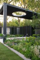 A louvered timber cloister above a circular pond. Plants including Geranium phaeum, Iris sibirica 'Tropic Night', Euphorbia, Anthriscus sylvestris 'Ravenswing' -Queen Anne's Lace and Dicentra formosa. The Cancer Research UK Garden, Gold Medal Winner RHS Chelsea Flower Show 2010
 