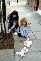 Mother and child guerrilla gardeners planting bulbs in a tree pit in a Hackney street, London