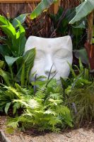 Head sculpture 'Bindi Dreamer' by Jilly Sutton, nestling amongst green foliage of Cyperus papyrus and Dryopteris filix-mas - The Yoga Garden, Bronze medal winner at the RHS Hampton Court Flower Show 2010