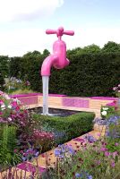 Path with pink glass tiles leading to a seating area next to a pond with a pink tap water feature, planting include Agapanthus 'Dr Brouwer', Cosmos, Geranium psilostemon and Knautia macedonica - 'A Matter of Urgency', Silver Gilt medal winner - RHS Hampton Court Flower Show 2010 