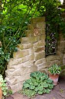 Recycled stone wall with decorative panel and Hostas in pots
