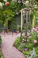 Seating area, gravel path, wooden obelisk and borders with Rosa 'Gertrude Jekyll' in pretty secluded suburban garden - High Trees, Longton, Stoke-on-Trent, Staffordshire, NGS