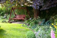 Garden with Wooden swinging bench in shadey area. Hosta and Digitalis in borders