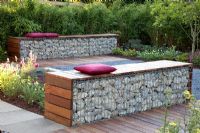 Small garden with patio and benches made from wood and gabions backed by Fargesia murielae - Bamboo hedge
 