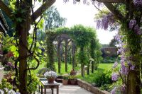 Late spring garden with pergola on lawn viewed through Wisteria covered pergola on terrace. Dawn End Lodge NGS, May 
 