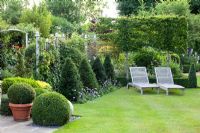 Country garden with loungers on lawn. Taxus - Yew pyramids, trained Capinus betulus - Hornbeam trees, Ligustrum and Buxus balls
