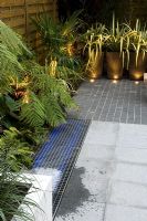 Small urban courtyard garden with Phormium in containers and uplighting