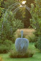 Wooden apple sculpture underplanted with ornamental grasses and rustic arch in background