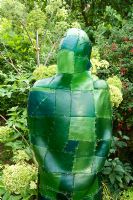 Green resin figure in border with Angelica behind. Yulia Badian garden, London, UK 
 