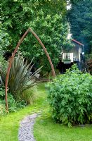 Urban garden with metal arch over slate path. Border with Phormium -New Zealand Flax. Yulia Badian, London, UK
 