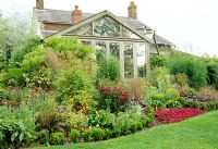 Summer border and conservatory. Fovant Hut Garden, Wilts