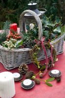 Christmas basket of natural folilage of holly, rosehips, ivy berries, pine cones, Viburnum with rustic wreath, mistletoe and candles

