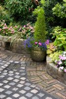 Path and wall made from reclaimed cobbles and bricks with classical container and mixed late summer bed with standard Fuchsia, Begonia, Heuchera and Choisya - Brocklebank Road, Southport, Lancashire NGS 
