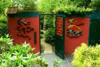 Three-Friends-of-Winter garden has a winter flowering plum, Prunus mume, at its centre and Sasa veitchii - Bamboo. Hand carved Phoenix and dragon flank gate into Red Wall Garden. Beggars Knoll, Newtown, Westbury, Wiltshire, UK